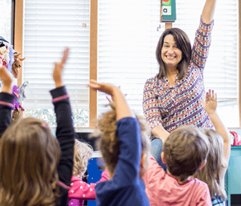 A happy teacher has her students raise their hands and all of them copy her
