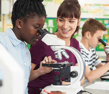 science teacher working with student who is looking in a microscope