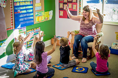 preschool teacher interacts with group of young kids