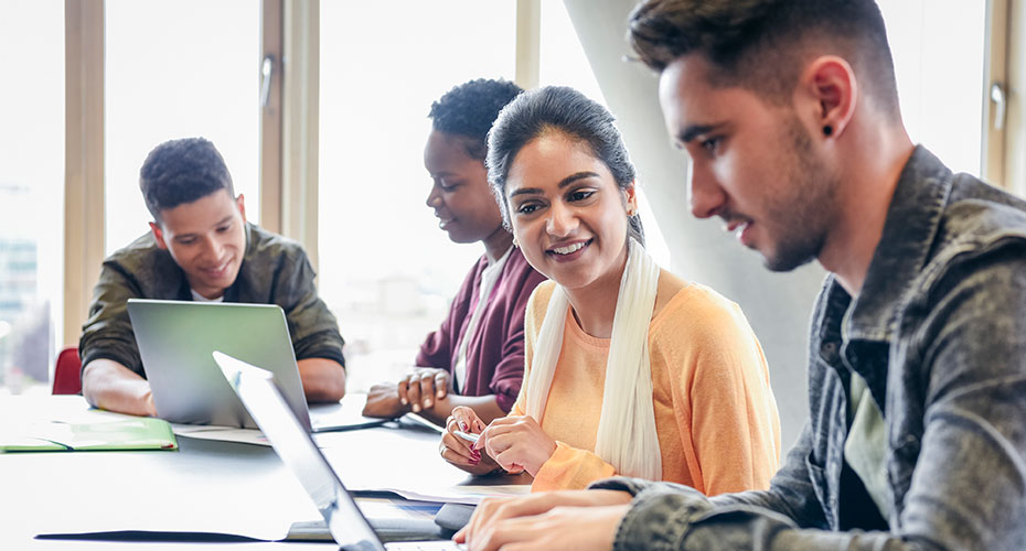four foreign students study on laptops together
