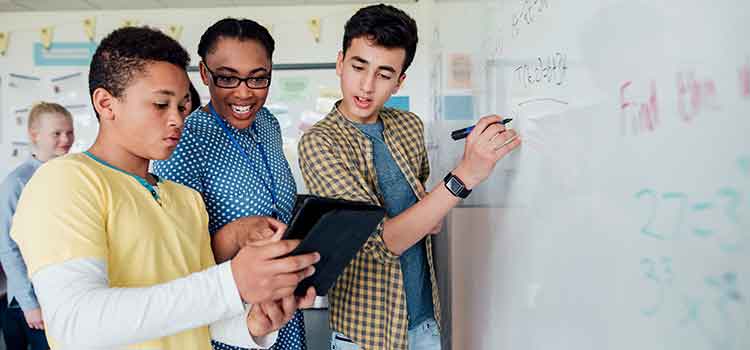 teacher instructing two high school students at whiteboard