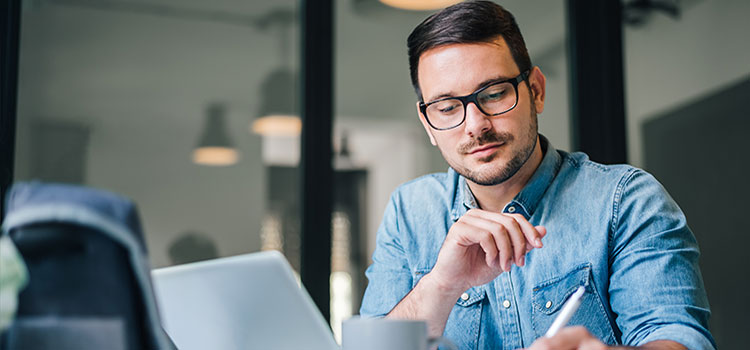 man doing research and taking notes on laptop