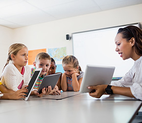 woman teacher goes over lesson on tablet with kids