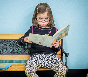 young girl sitting on bench reading a book
