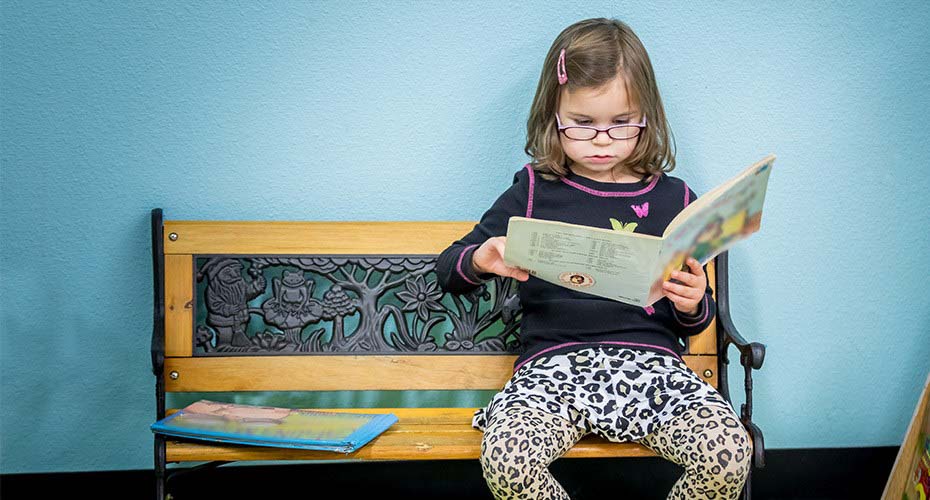 young girl sitting on bench reading a book