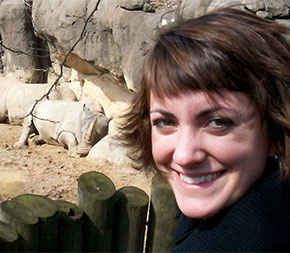 smiling woman standing in front of rhinoceros exhibit at the zoo