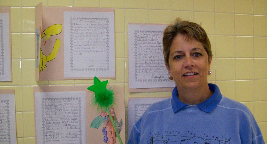 special education teacher in classroom next to student papers hanging on wall